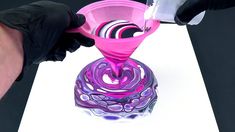 a person in black gloves is pouring liquid into a pink glass vase on a white surface