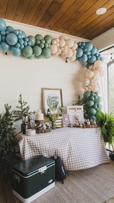 a table topped with balloons and other decorations next to a window filled with potted plants