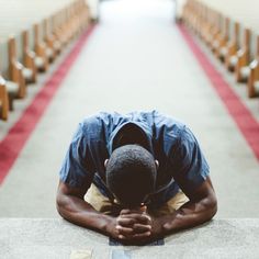 a man sitting on the ground in front of rows of pews with his head down