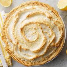 a lemon pie on a white plate next to sliced lemons and a striped napkin