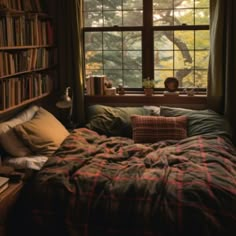 an unmade bed in front of a window with bookshelves on either side