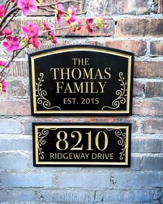 two black and gold signs on a brick wall with pink flowers in the foreground