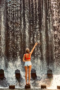 a woman standing in front of a waterfall pointing at the water coming out of it