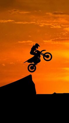 a person on a dirt bike doing a trick in the air at sunset or sunrise