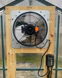 a fan mounted on the side of a wooden wall in front of a greenhouse door