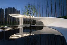 an artistic sculpture in the middle of a pond with trees and buildings in the background