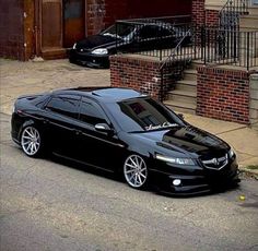 a black car parked on the side of a road next to a brick building and stairs