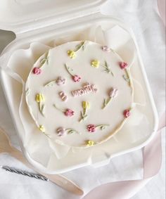 a white cake with pink and yellow flowers on it sitting in a box next to a knife