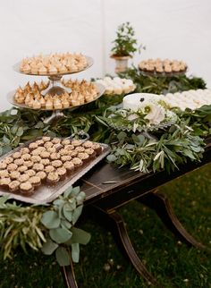 an assortment of desserts are displayed on a table with greenery and white flowers