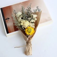 a bouquet of white and yellow flowers tied to a brown paper with a book in the background