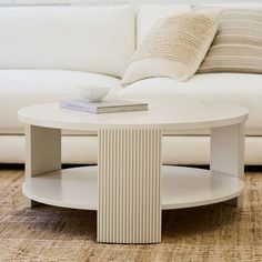 a white coffee table sitting on top of a rug in front of a couch with pillows