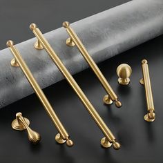 four brass handles and six pulls on a black surface with grey fabric behind them,