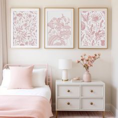 a bedroom with pink flowers on the wall and two framed pictures above the bed, along with a white chest of drawers