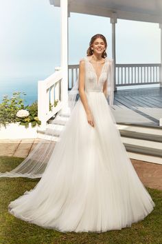 a woman in a white wedding dress standing on the grass near some steps with her arms behind her back