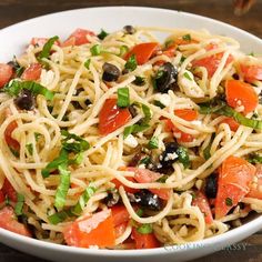 a white bowl filled with pasta and veggies on top of a wooden table