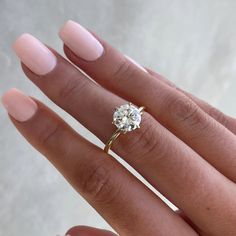 a woman's hand with a diamond ring on her finger and pink manicured nails