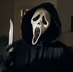 a person in a black hooded jacket holding a knife and wearing a white scream mask