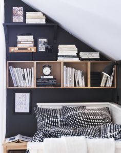 a bed with black and white sheets, bookshelves and a clock on the wall