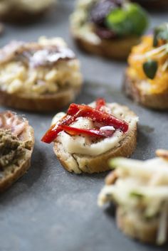 small appetizers with various toppings on them sitting on a baking sheet, ready to be eaten