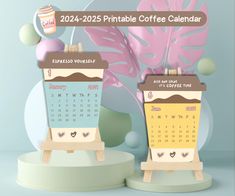 two calendars sitting on top of wooden easers next to a plant and cup