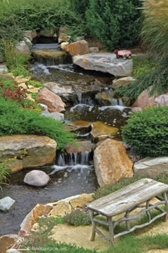 a wooden bench sitting next to a small waterfall in a garden with rocks and grass