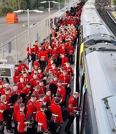 a large group of people in red uniforms are standing next to a train on the tracks