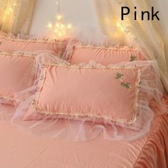 a bed with pink sheets and pillows in front of a curtained window, with fairy lights on the wall behind it