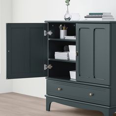 an armoire with two doors and drawers on the bottom shelf, in front of a white wall