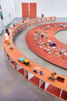 an orange circular table with many books on it in a room filled with white columns