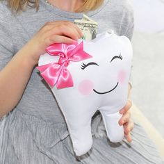 What an adorable way for a child to store her tooth for the night the tooth fairy visits. This charming tooth shaped pillow makes it a sure way for the tooth fairy's treasures to find their way to the recipient with its small hidden pocket. It shares a happy smiling face with a cute pink satin bow on top and is sure to please any little girl. The pillow features a pocket at the top which is just the right size for teeth and coins. Pillow measures 7.5 inches high x 6.75 inches wide. Tooth Fairy Gifts, Lillian Rose, Teeth Shape, Pocket Pillow, The Tooth Fairy, Shaped Pillow, Tooth Fairy Pillow, Smiling Face, Favor Bag