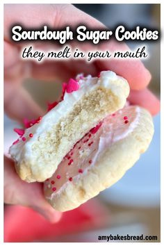 someone holding a half eaten sugar cookie with pink sprinkles and white frosting