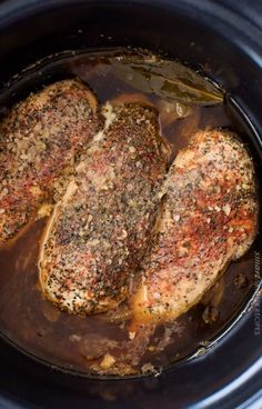 two pork chops in a slow cooker with brown sauce and seasoning on top