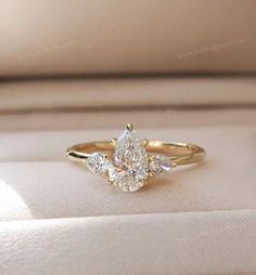 an engagement ring with three pear shaped diamonds on it's side in a box