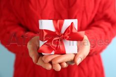 a person in a red sweater holding a white gift box with a red ribbon on it