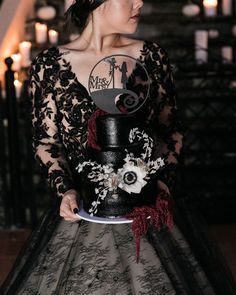 a woman in a black dress holding a cake with white and red flowers on it