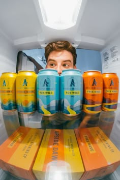 a man is looking through an open refrigerator with six cans of beer in front of him