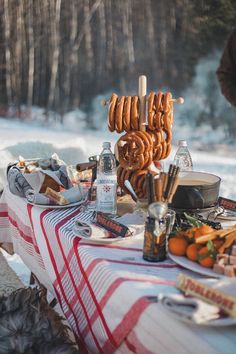 an outdoor picnic table with hot dogs and drinks on it, in the winter snow