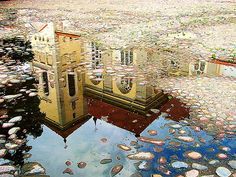 the reflection of an old building in a puddle of water with rocks on the ground