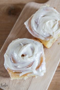 two glazed donuts sitting on top of a wooden cutting board