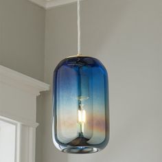 a blue glass light hanging from a ceiling in a room with white walls and windows