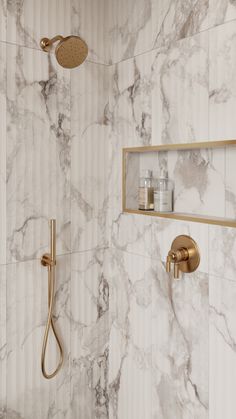 a bathroom with marble walls and flooring, gold faucet shower head and handset