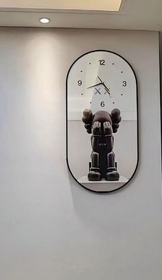 a clock mounted to the side of a white wall next to a black bear statue