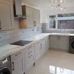 an empty kitchen with grey cabinets and marble counter tops, washer and dryer in the foreground