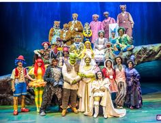 a group of people dressed in costumes posing for a photo on stage with an audience