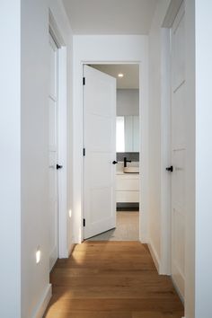 an empty hallway with white doors and wood flooring