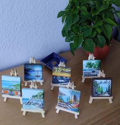 small easels with paintings on them sitting on a table next to a potted plant