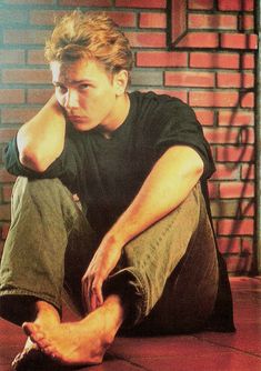 a young man sitting on the floor with his foot up to his face and hands behind his head