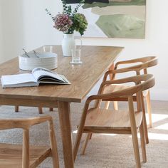 a wooden table with two chairs and a book on it, in front of a painting