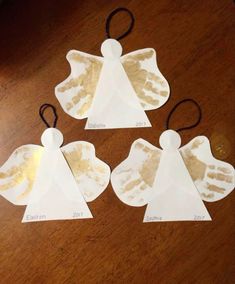 three angel ornaments made out of paper on a wooden table