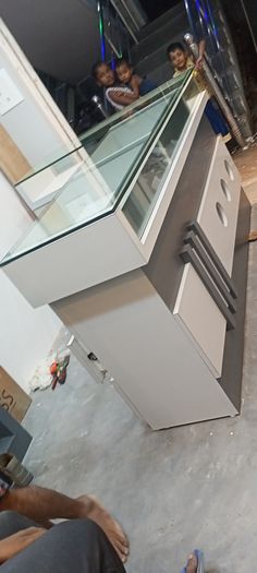 two people sitting on the ground looking down at something that looks like a cabinet with glass doors